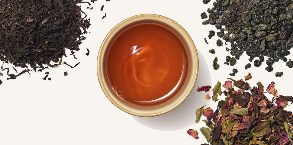 Organic black tea, gunpowder green, matcha toasted rice, and white rose tea ingredient piles surround a cup of brewed tea.